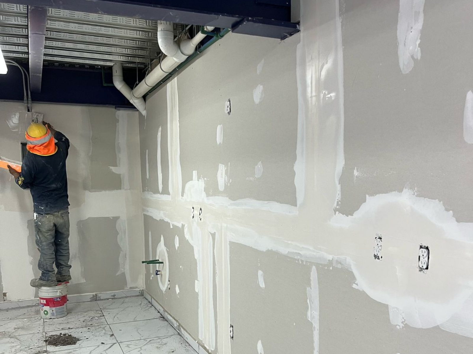 Trabajador de la construcción realizando el acabado y resanación de muros de tablaroca en un proyecto de remodelación de oficinas corporativas.