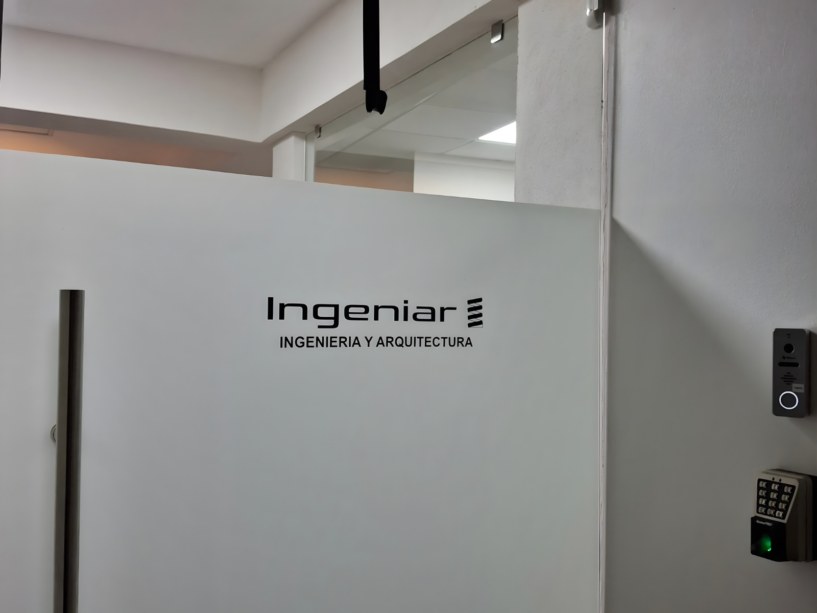 Logotipo de "Ingeniar - Ingenieria y Arquitectura" rotulado en vinil negro sobre una puerta de cristal esmerilado en la entrada de una oficina.